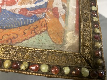 A Tibetan thangka in inlaid gilt brass frame, 19th C.